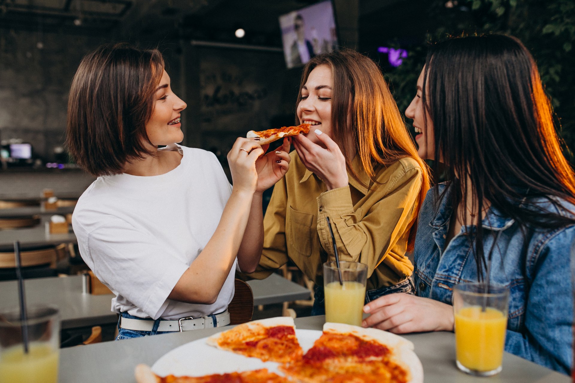 Trzy przyjaciółki jedzą pizzę w przytulnej restauracji