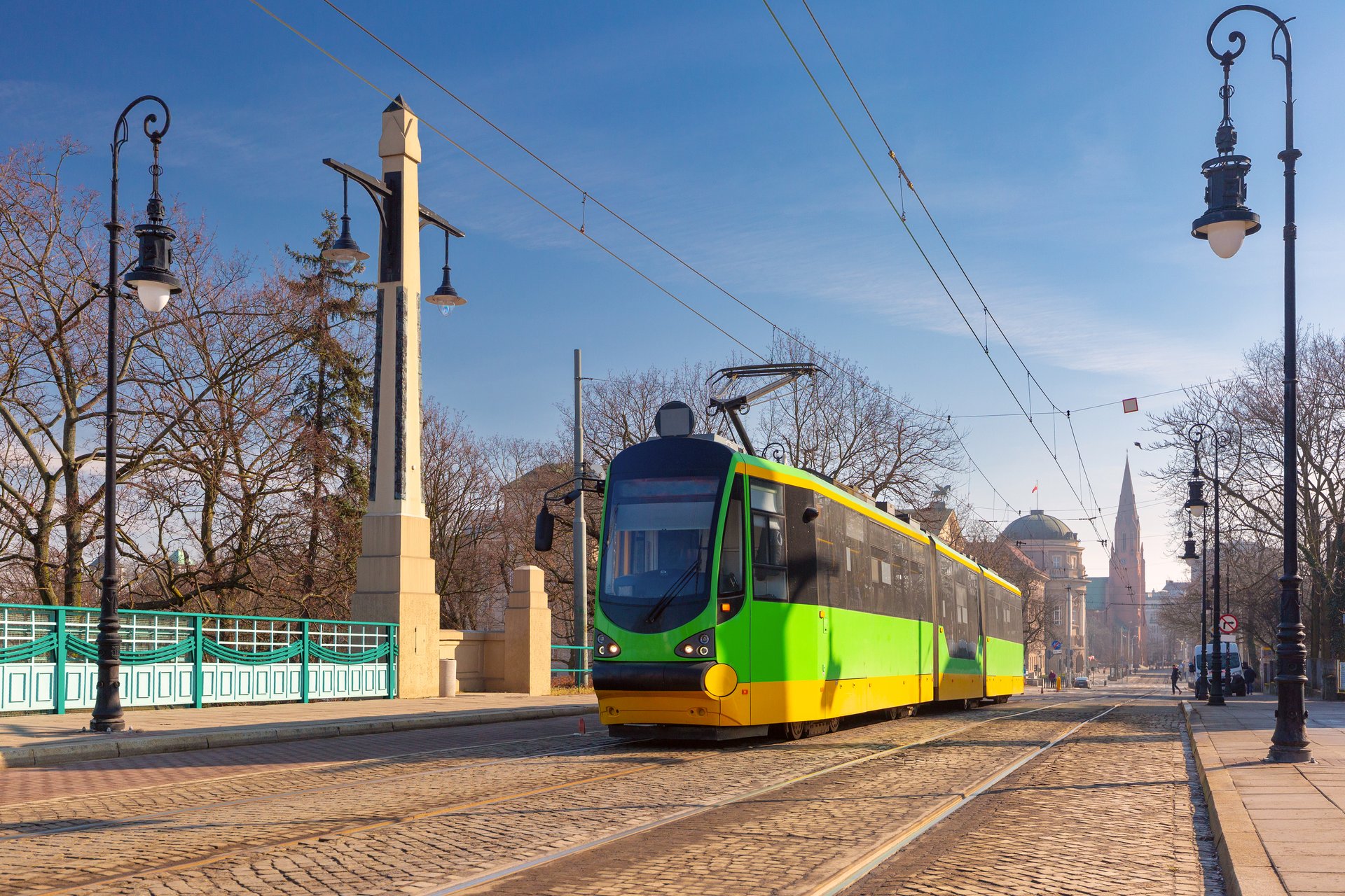 Zielono-żółty tramwaj przejeżdża przez zabytkowy most w centrum Poznania