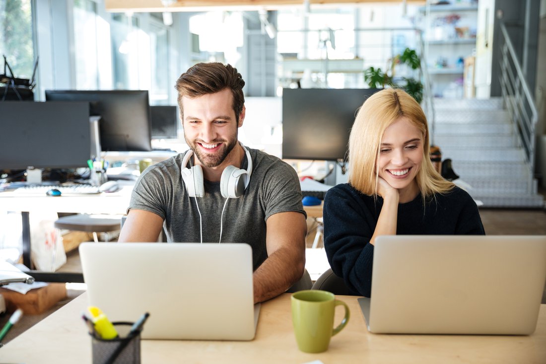 Uśmiechnięci młody mężczyzna i kobieta pracują przy laptopach w biurze