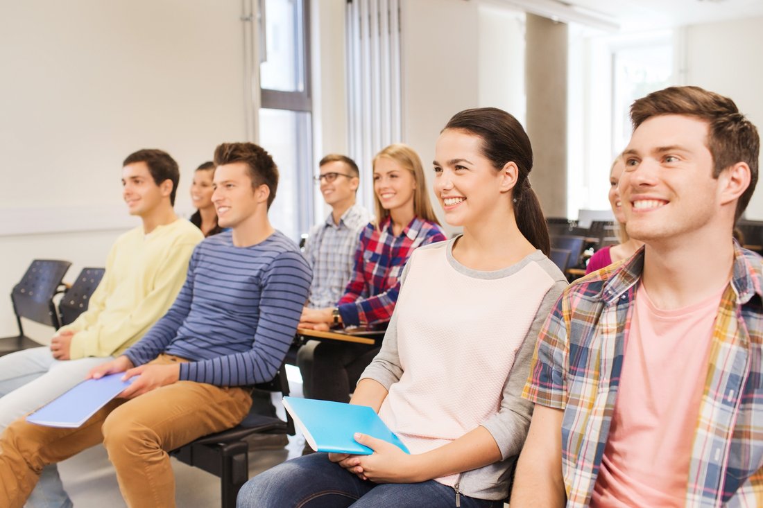 Uśmiechnięci studenci z notatnikami słuchają wykładu w jasnej sali